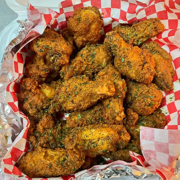 A close-up of Krab Kingz's fried seafood, seasoned with herbs and spices, in a red and white checkered paper-lined container.