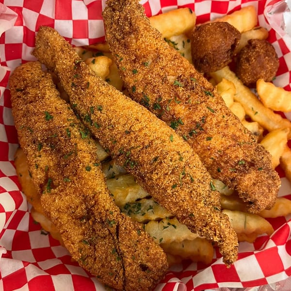 Three crispy fried fish fillets with french fries and hush puppies in a red and white checkered basket.