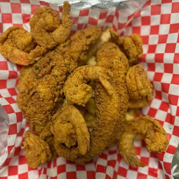 A close-up of golden-brown fried shrimp and fish pieces in a red and white checkered paper-lined basket.